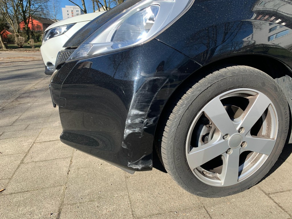 Frontschaden links an schwarzem Fahrzeug – Stoßfänger aufgerissen mit weißem Fremdlack